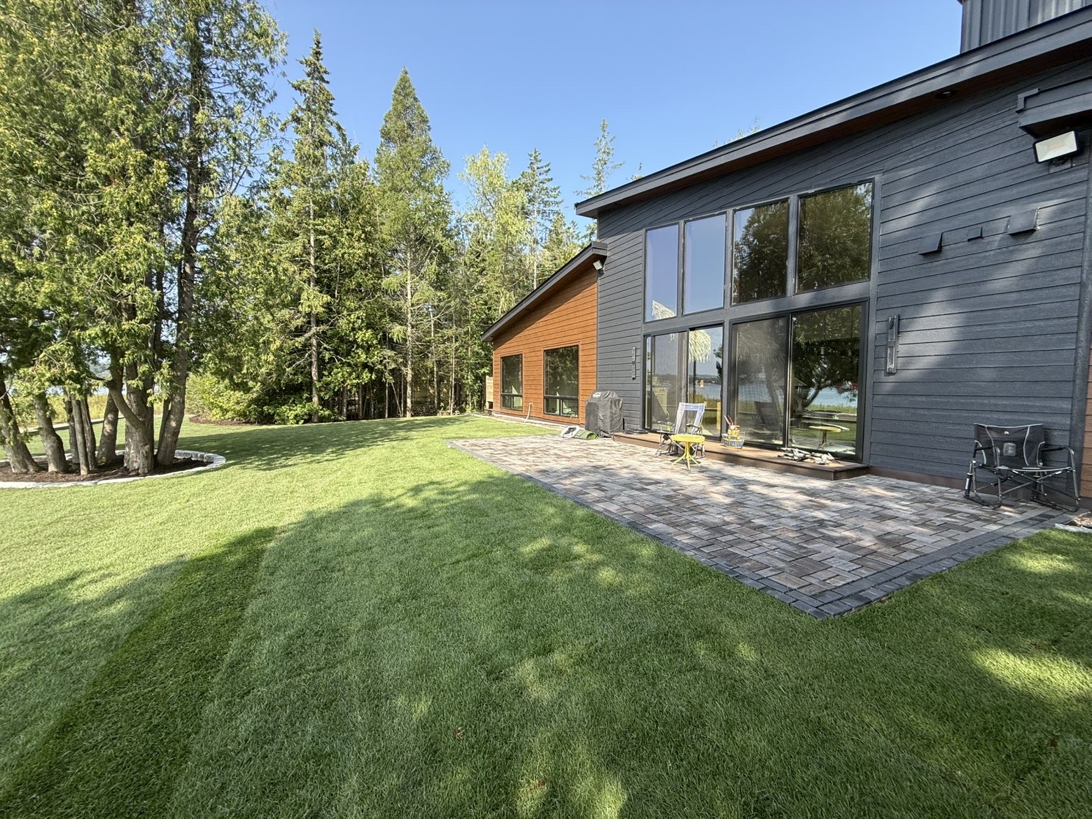 Backyard paver patio and finished lawn beside a modern Door County home
