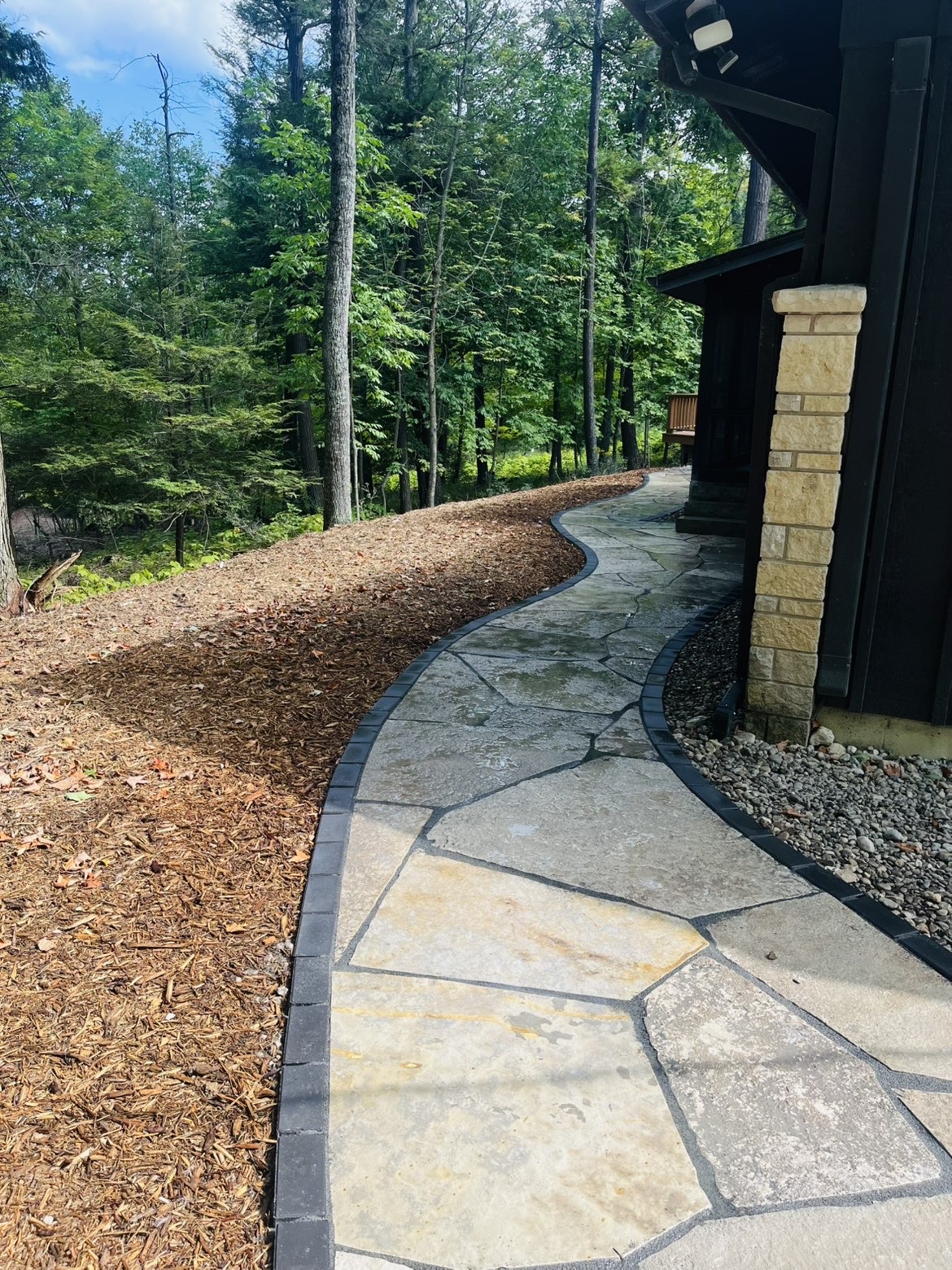 Curved natural flagstone walkway with dark paver edging at a wooded Door County home